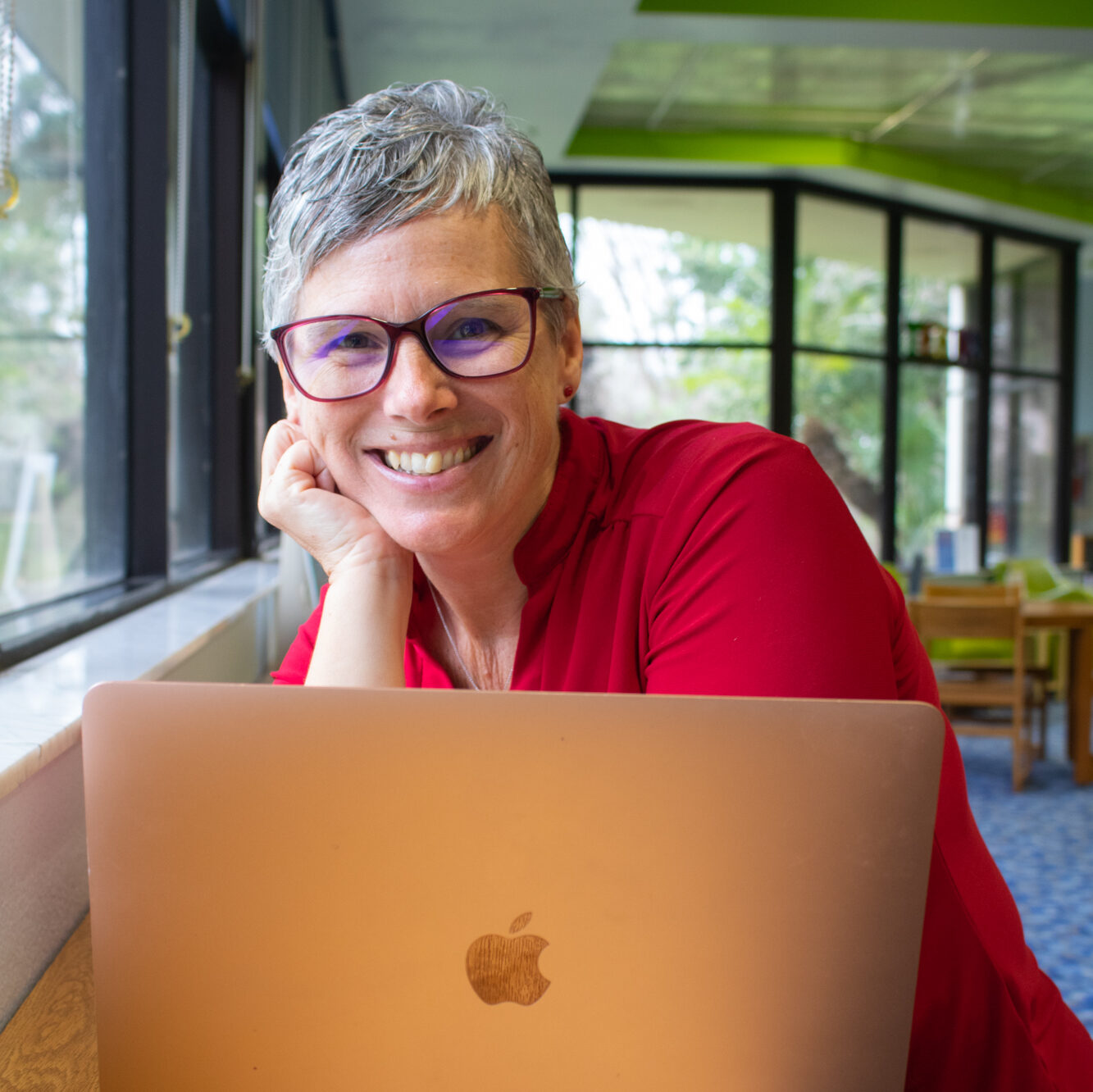 Amy Levesque portrait, red polo shirt, smiling in front of open laptop